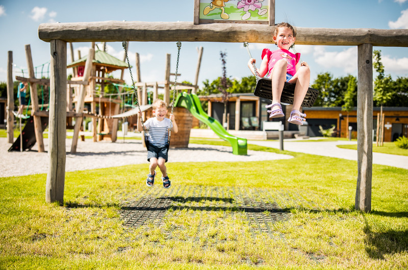 schaukelnde Kinder am Kinderspielplatz bei den Thermen Chalets